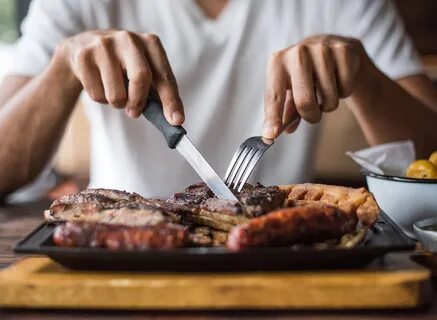 man cutting into steak with fork and knife. 