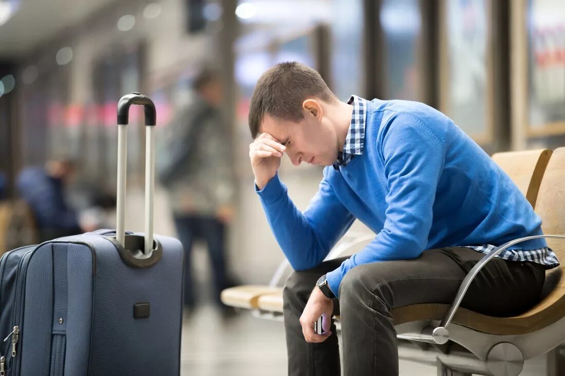Уставшие туристы. Пассажиры в аэропорту. Сижу на чемоданах. Люди в аэропорту. Человек с чемоданом.