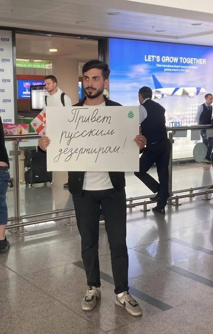 Почему сбежали из россии. Мужчина встречает в аэропорту. Плакаты встречающих в аэропорту. Как встречают в аэропорту. Люди в аэропорту.