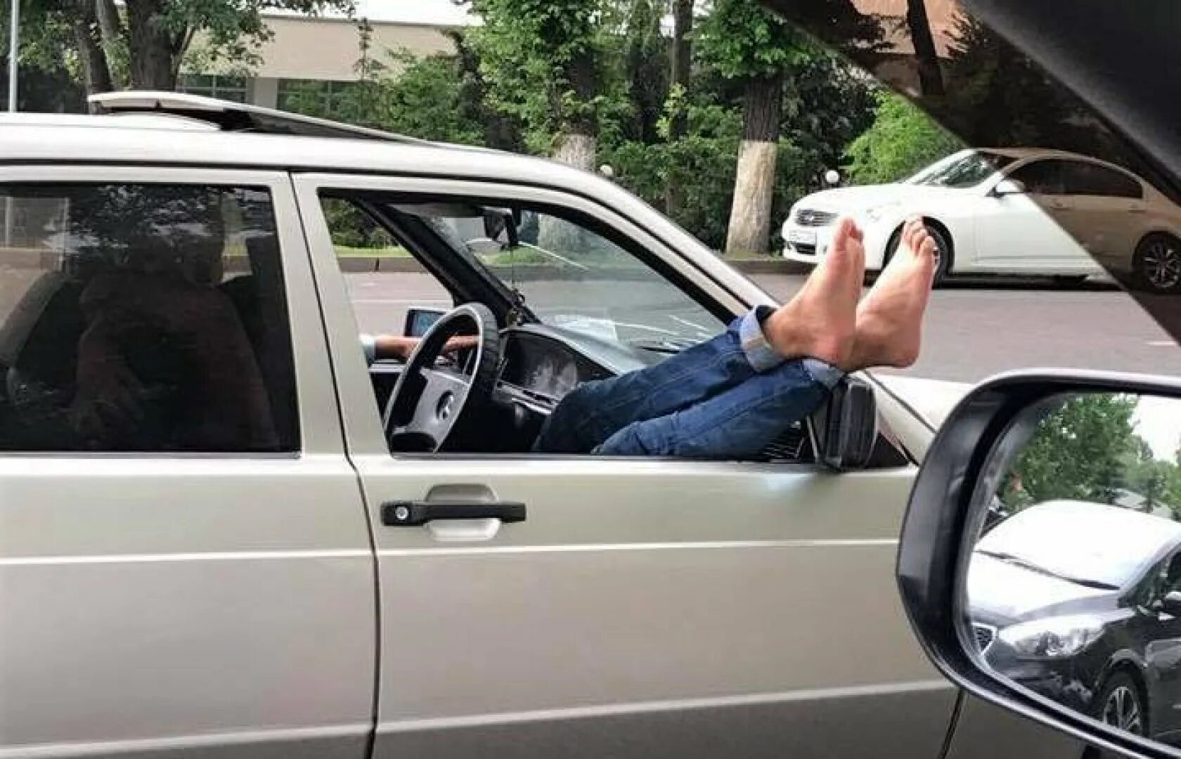 Человек высовывается из окна машины. Высунул руку из окна машины. Ноги в окно авто. Человек в машине.