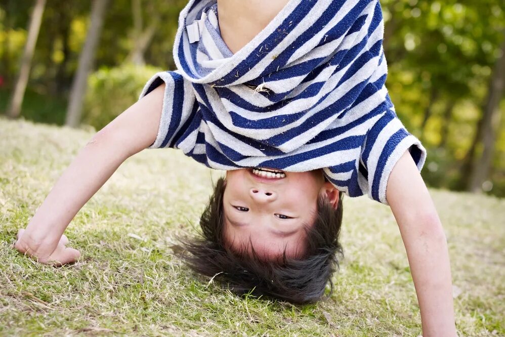 ребенок стоит на руках. мальчик вверх ногами. ребенок вверх ногами. мостик девочки. стойка на руках на траве.