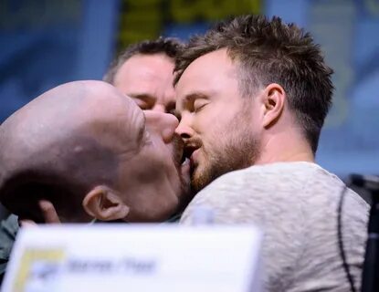 Actor Bryan Cranston watches actor Aaron Paul kiss a Walter White face mask...