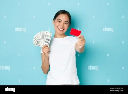 Happy carefree asian girl in white t-shirt holding cash but choosing credit...