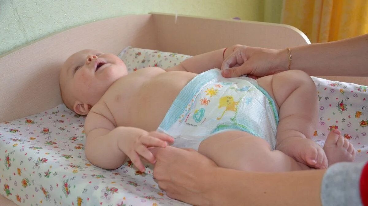 Ребенку меняют подгузник. Одевание памперса грудничку. Правильное одевание памперса новорожденному.