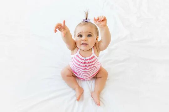 Малыш сидит. Малыш улыбается. Малыш сидит в памперсе. Младенец с поднятой рукой. Raise babies.