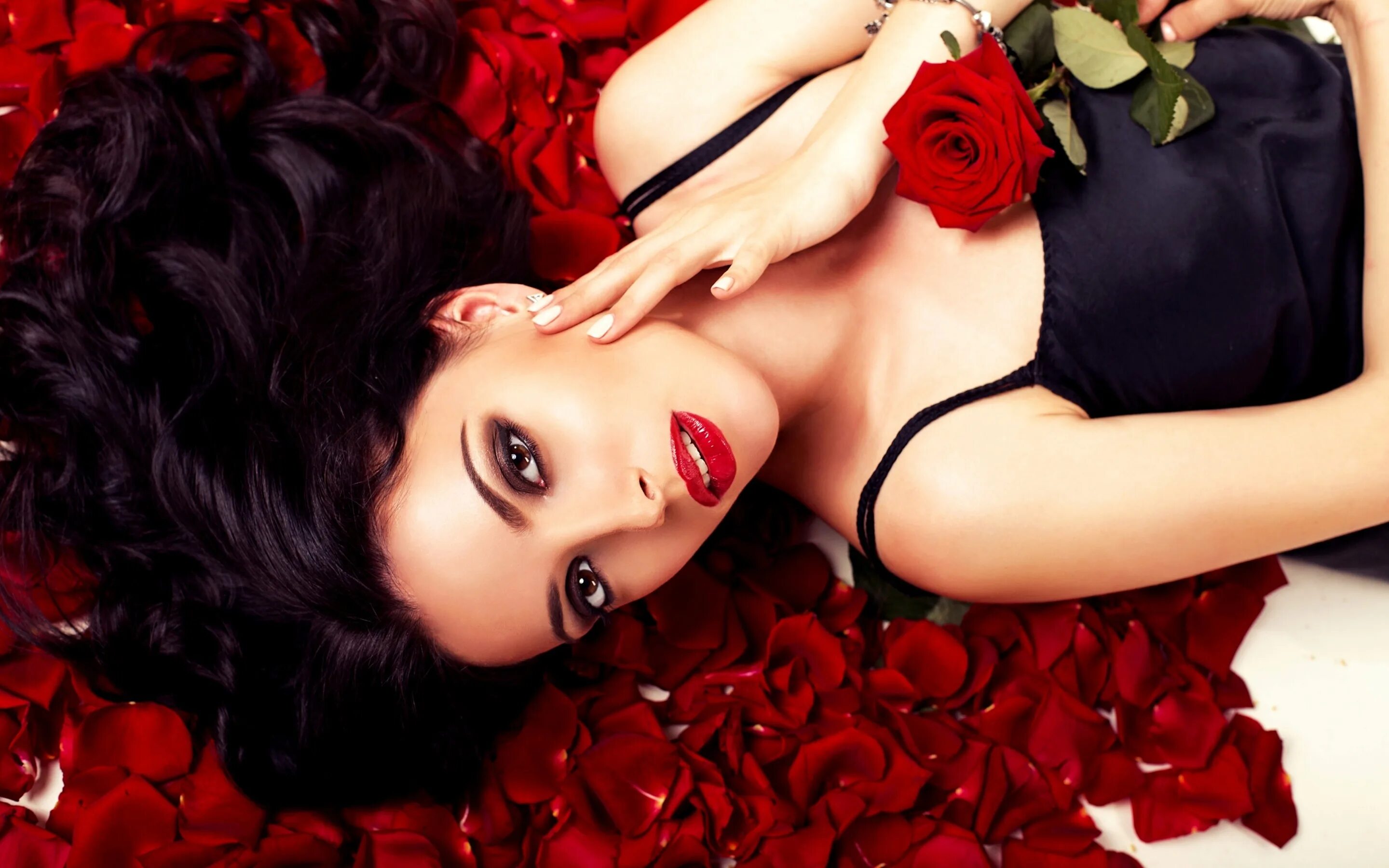 Брюнетки лежа. Девушка с красными розами. Роскошная женщина. Фотосессия с лепестками роз. Девушка брюнетка.
