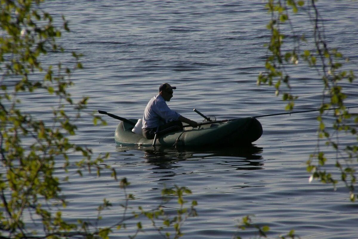 Рыбак используя моторную лодку проходит. Рыбак в лодке. резиновая лодка на озере. рыбак на резиновой лодке. надувная лодка на озере.