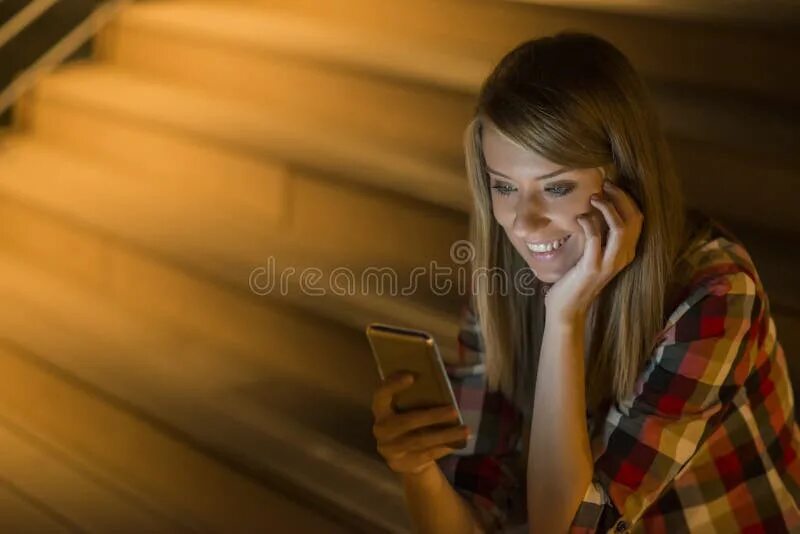 Бывшая читает смс. Девушка с телефоном улыбается. Молодая женщина с телефоном. Девушка улыбается смотря в телефон. Девушка улыбающая в телефоне.