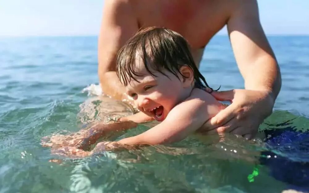 Маленький мальчик купаться. Купание детей в море. Купаться в море. Учиться плавать на море. Детки купаются в море.