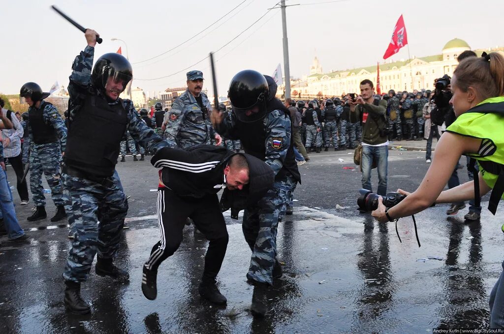 Полицейский бьет дубинкой.