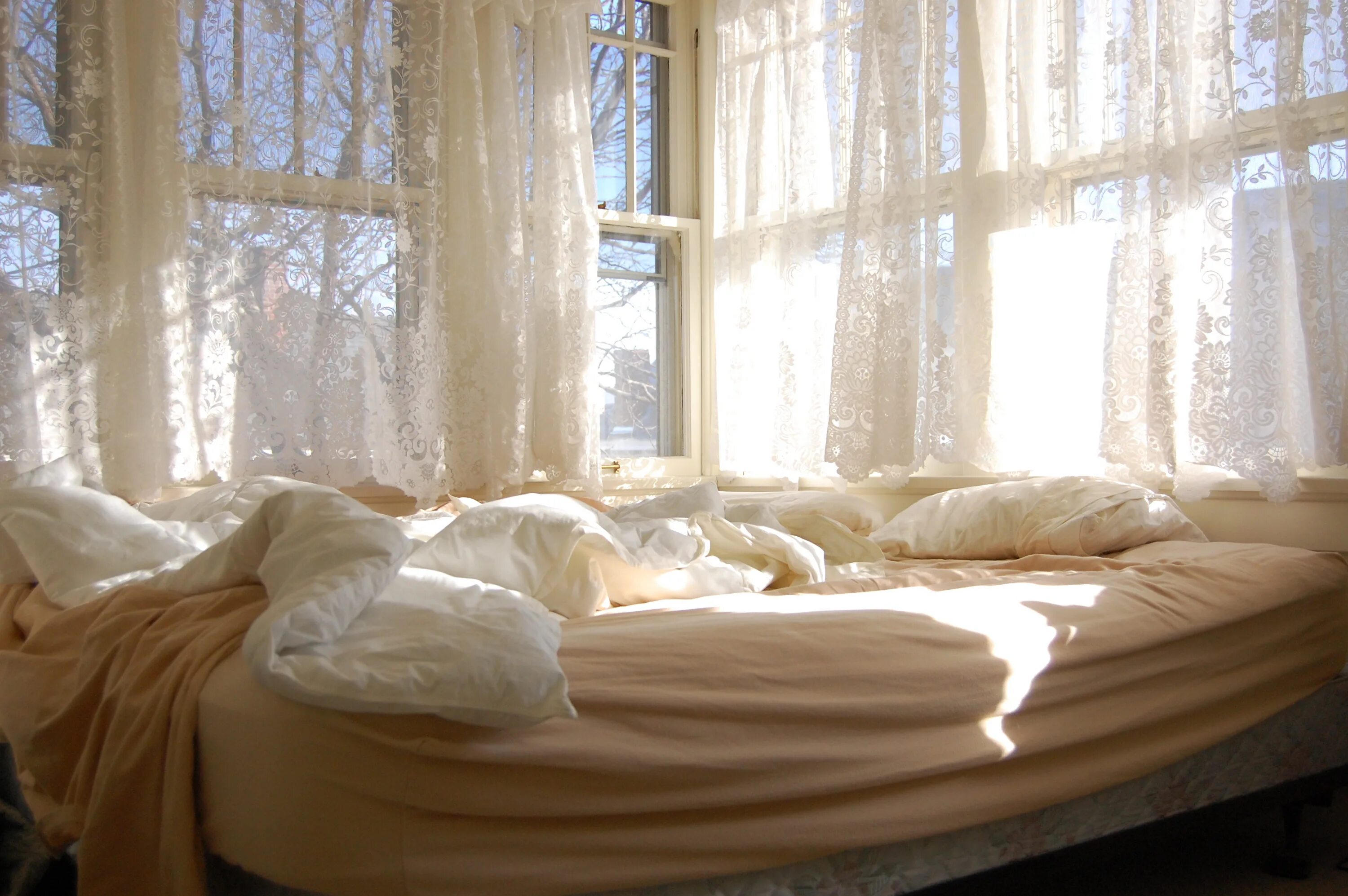 Уютная кровать. Кровать рядом с окном. Утренний свет в комнате. Кровать возле окна.