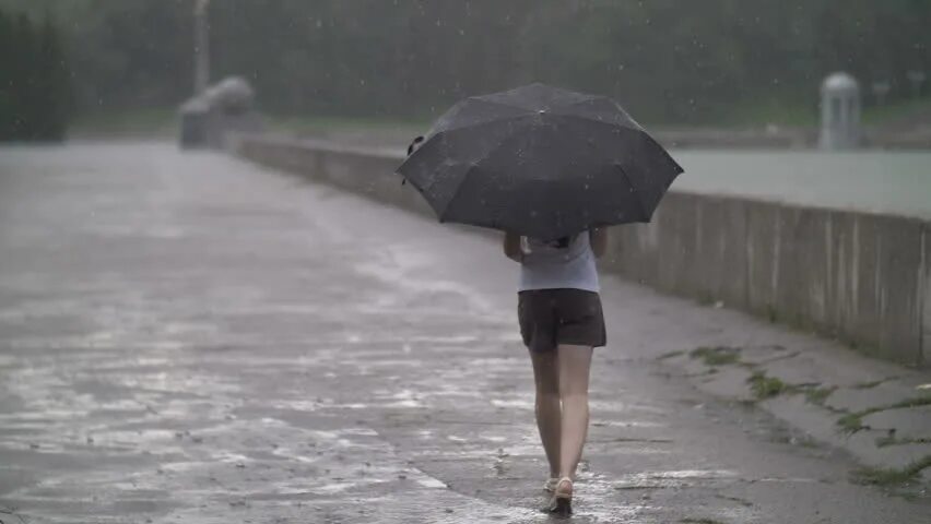 Girl Walking through a strong Rain in a small City with her Umbrella Unopen and kept down. Am walking in the rain