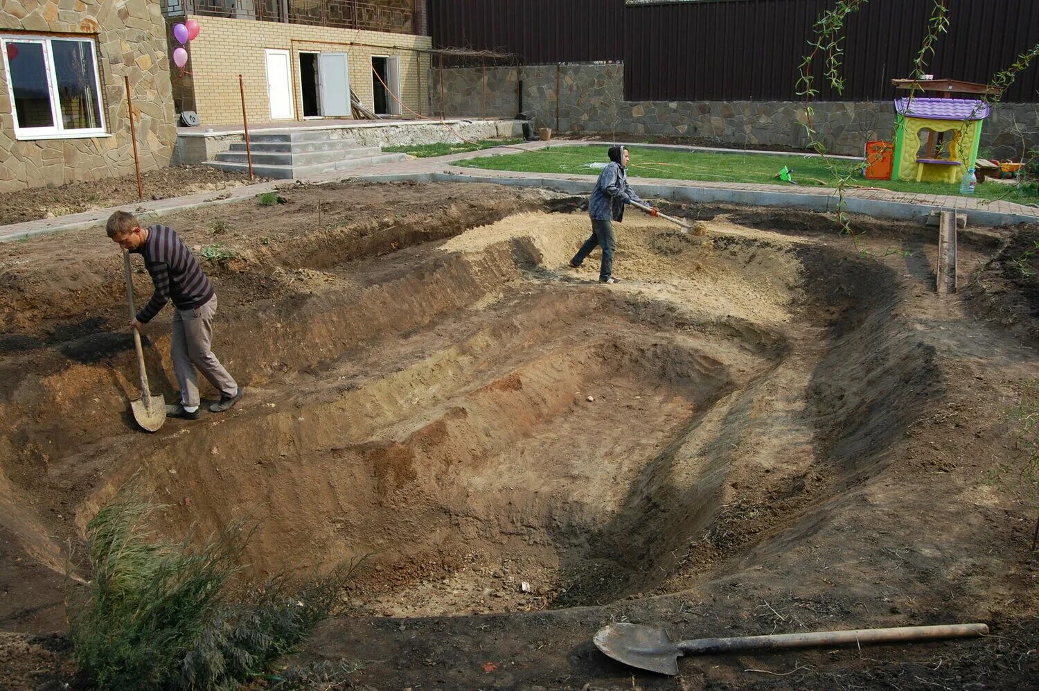 Подготовительные работы в строительстве. Выемка грунта. Разнорабочие. Рабочие на стройке. Экскаватор роет землю.