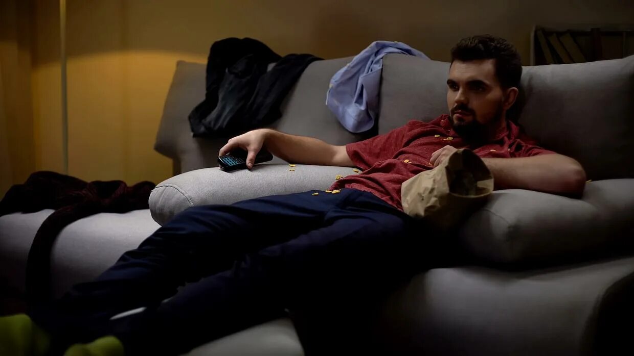 Сон сидеть на мужчине. Лежит на диване и ест. Мужик на диване перед телевизором. Человек лежит на диване с чипсами. Диван для одинокого мужчины.