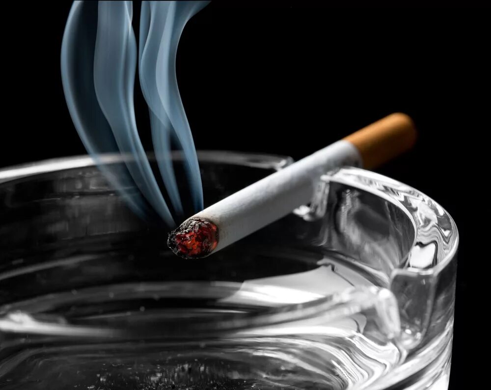 Тлеющая сигарета. Пепельница с сигаретой. Табачный дым. Пепел сигареты. Не потушит боль сигаретный дым дорогой коньяк
