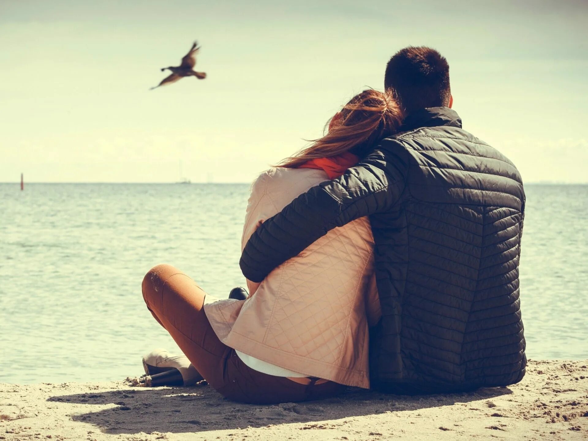 Двое влюбленных сидят на берегу. Обнимаются в море. Счастливые влюбленные. Мужчина и женщина на берегу. Sit on the beach