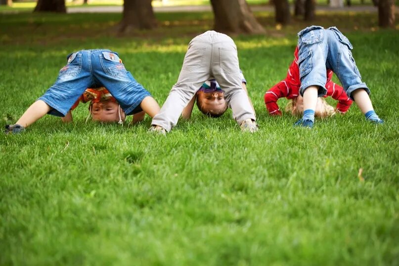 He enjoy playing. Кувыркаться в траве. Дети кувыркаются на зеленой траве. Ребенок стоит на голове. Ребенок вверх ногами.