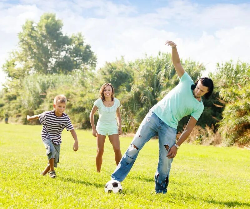 Семья играет в футбол. Подростки играют в мяч на природе.