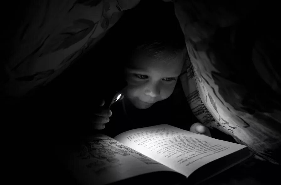 девочка с книгой подоодеялом. чтение в темноте. ребенок под одеялом ночью. читает под одеялом. читает под одеялом.