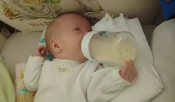 Съесть бутылочку. Кормление из бутылочки новорожденного. Позы для кормления бутылочкой. Ребёнок с бутылочкой для кормления в кроватке. Малыш с бутылочкой.
