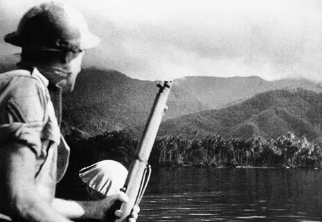 A helmeted Australian soldier, rifle in hand, looks out over a typical New Guinea...