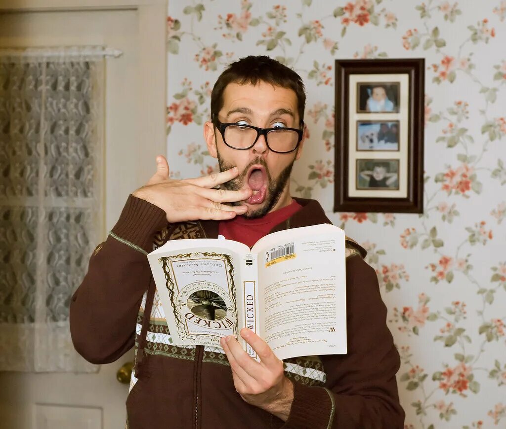 мужчина держит книгу в библиотеке. книга человек. книжка в руках. человек с книгой в руках. пацан с клавиатурой держит в руках.