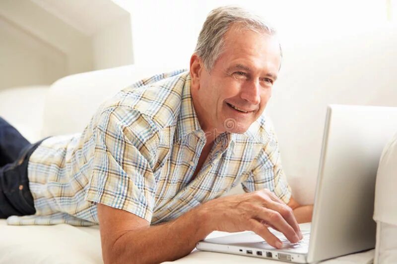 В скромно обставленном кабинете сидел пожилой человек. Пожилой мужчина с ноутбуком. Пожилой мужчина на диване. Пожилой мужчина за компьютером. Мужчина средних лет фото улыбается.