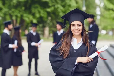 A young female graduate with a scroll in her hands is smiling against the b...