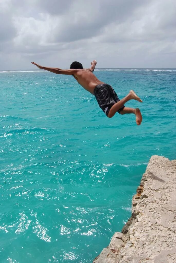 Прыжок в воду со скалы. Человек прыгает в море. В прыжке. Прыжки в воду.