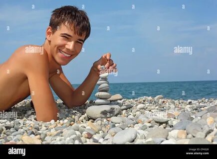 teenager boy lying on stony seacoast, creates pyramid from pebble Stock Pho...