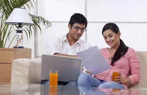 Young Couple Sitting On Sofa Using Laptop While Reading Document Photo Back...