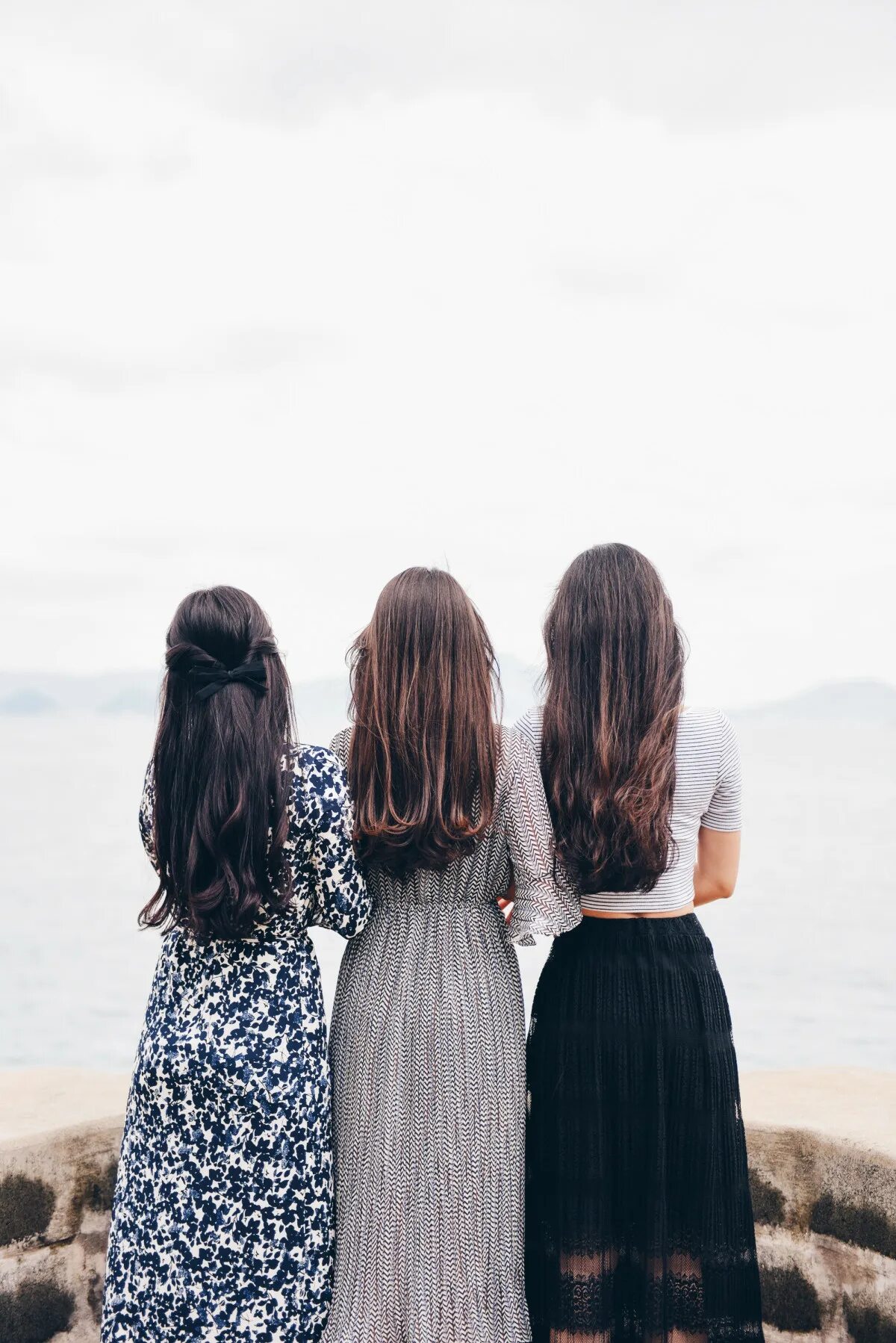 Рядом стоят 3 девушки. Фотосессия подруг. Три подруги с тёмными волосами. Три девочки со спины. Красивые подруги.