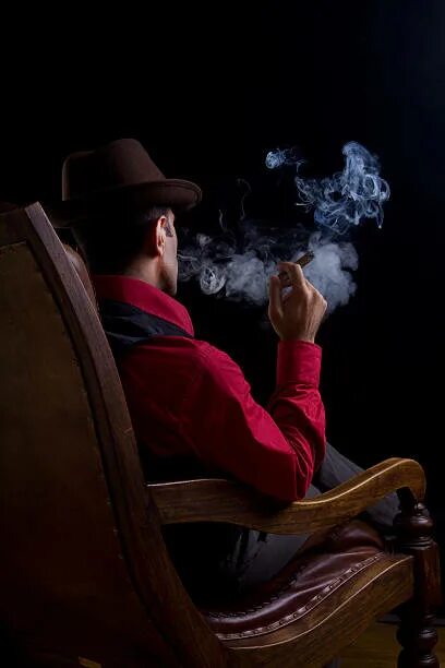 С сигарой на кресле качалке. Человек сидит на стуле и курит. Мужик на кресле качалке с сигарой. Чел сидит на кресле и курит. Виски шляпа