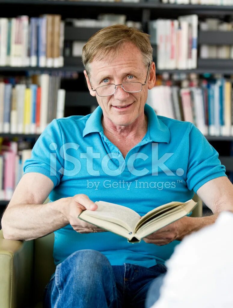 Мужчина в библиотеке. Пожилой мужчина с книгой. Пожилой мужчина в библиотеке держит книгу в руках. Старик в библиотеке.