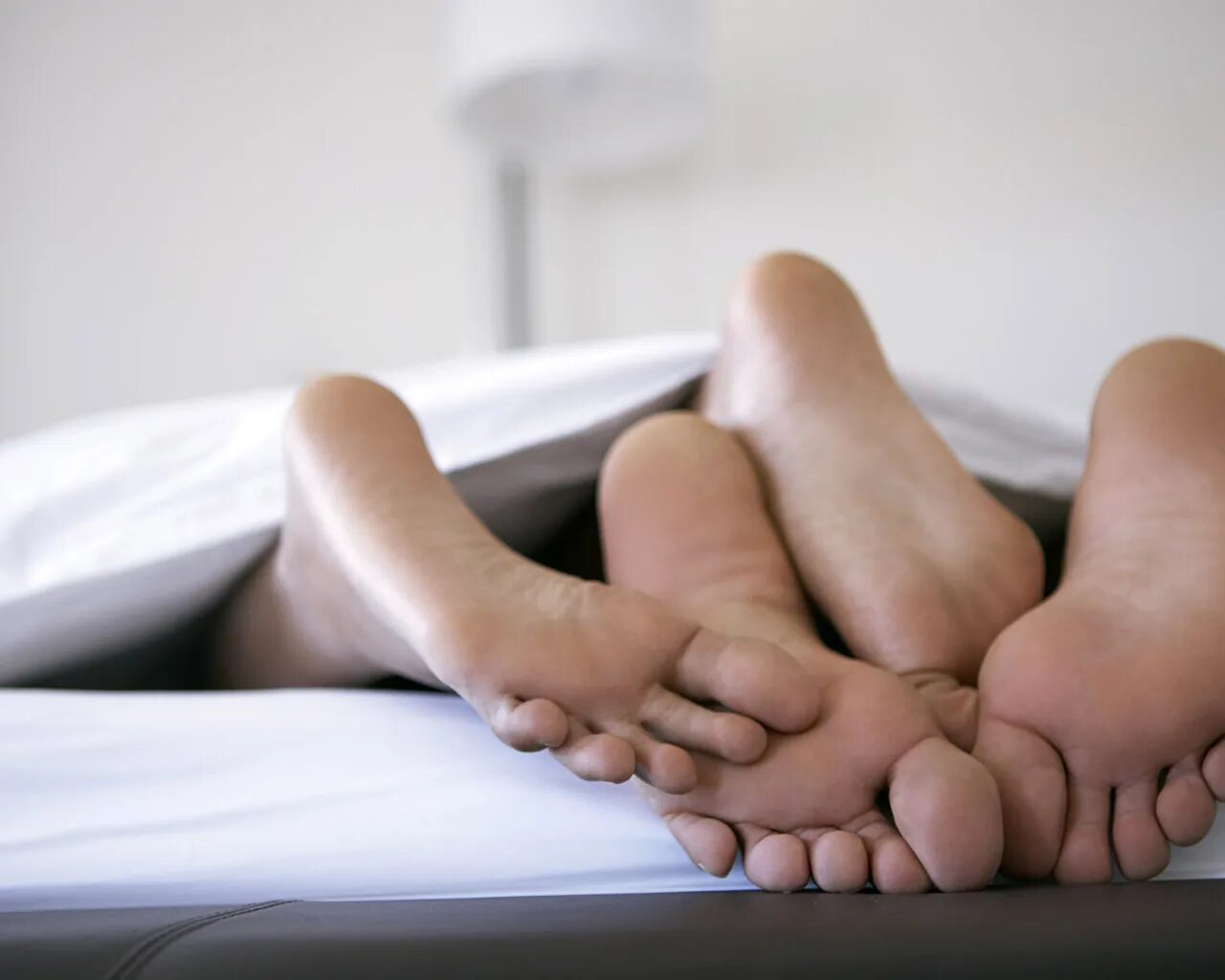 Контакт в постели. Мужские и женские ступни. Ноги на кровати. Пятки под одеялом. Мужские и женские ноги в кровати.
