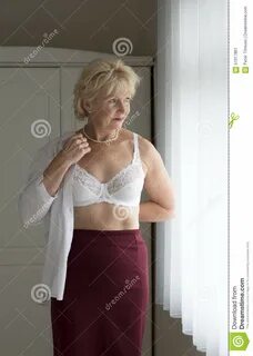 Пожилая женщина получая одетый надевать рубашка над белым бюстгальтером сто...