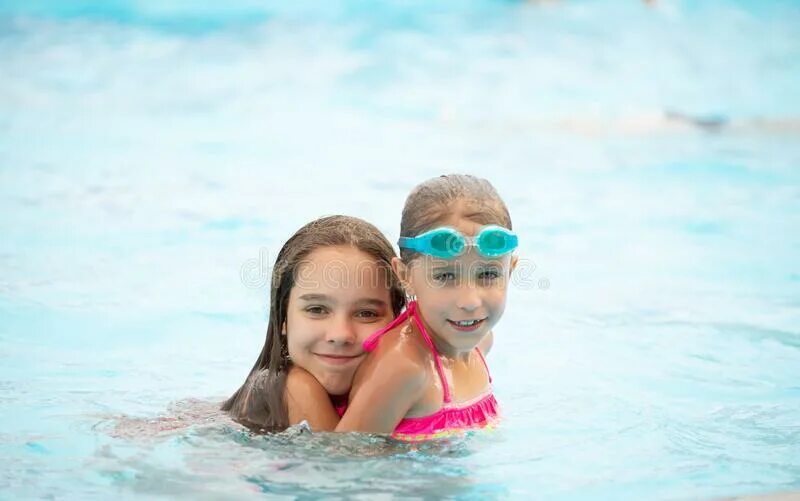 Две девочки плавают. Девочка маленькая в купальных очках. A girl Swims in the Pool and enjoys a Sunny Day.