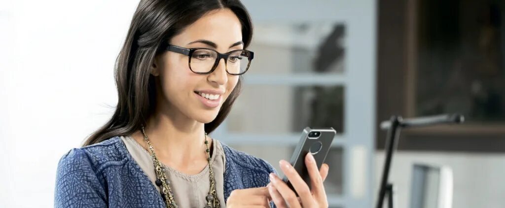 Девушка в очках в офисе. Держит очки. Очки бейтса. Очков для работы за компьютером. Успешная женщина.