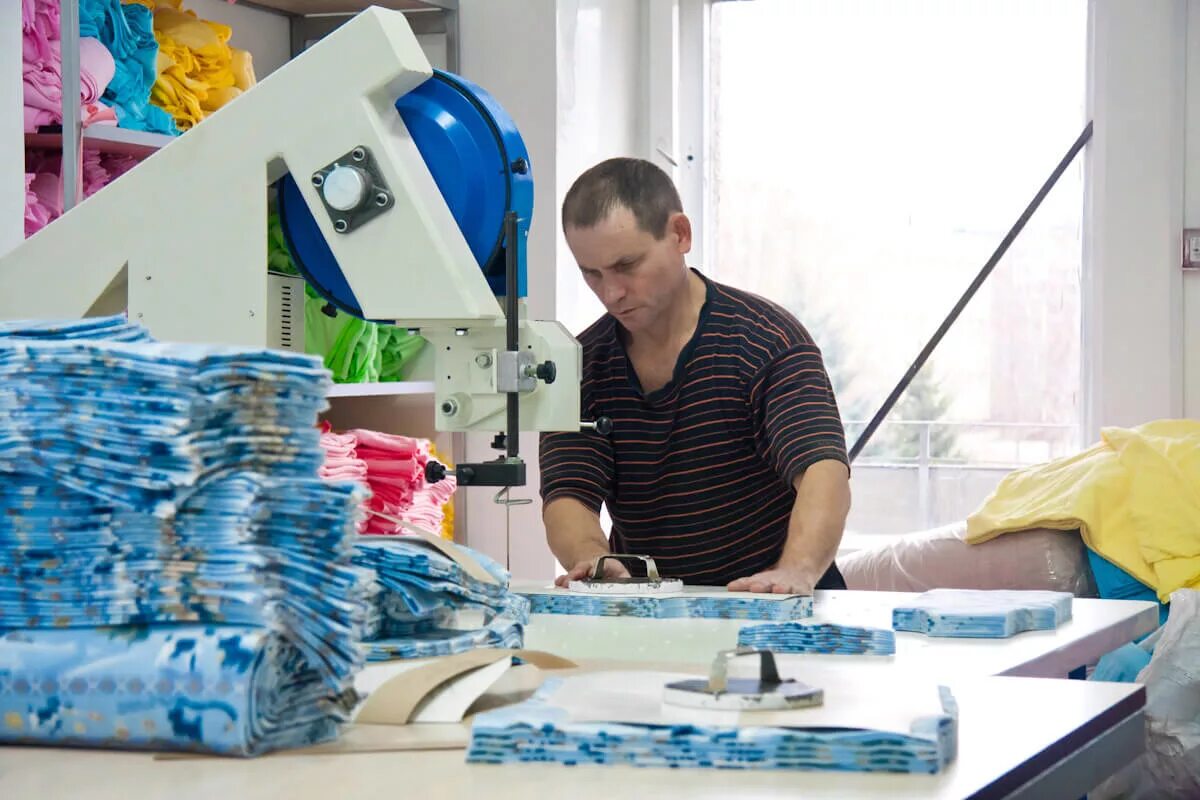 Машина для раскроя ткани. Раскройный цех на швейной фабрике. Раскройный цех швейного производства. Раскройщик ткани. Раскройный цех швейного производства.