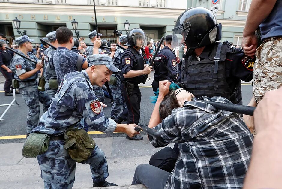 Полицейский бьет дубинкой.