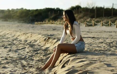 Girl in denim shorts sitting on a sand beach - 1900x1201.