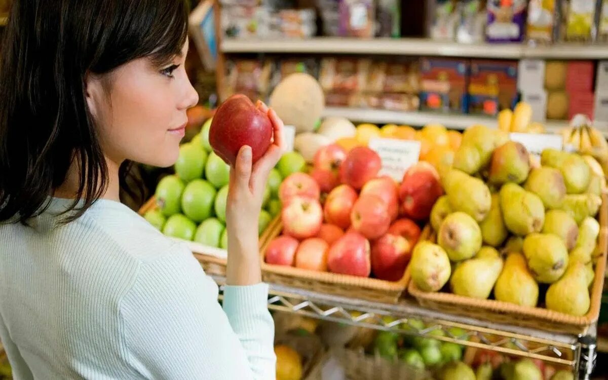 Употребление фруктов. Женщина на рынке выбирает овощи. Яблоко магазин. Яблоки на прилавке. Выбор продуктов.