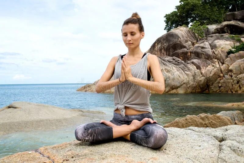 Йога остров. Девушка медитирует на Камне. Медитация камни. Картинка девушка на пляже медитирует. Девушка медитирует на море в шортах.