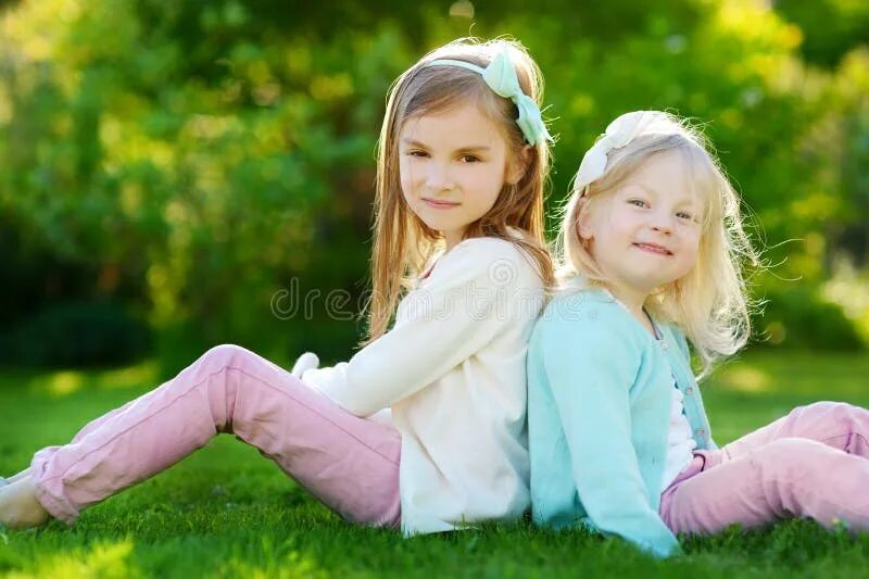 Little cunny two cute sisters laughing and playing in green sunny park, stock photo. Girl big sis. Cute little sister. Две сестрички веселятца. Две сестры обнимаются.