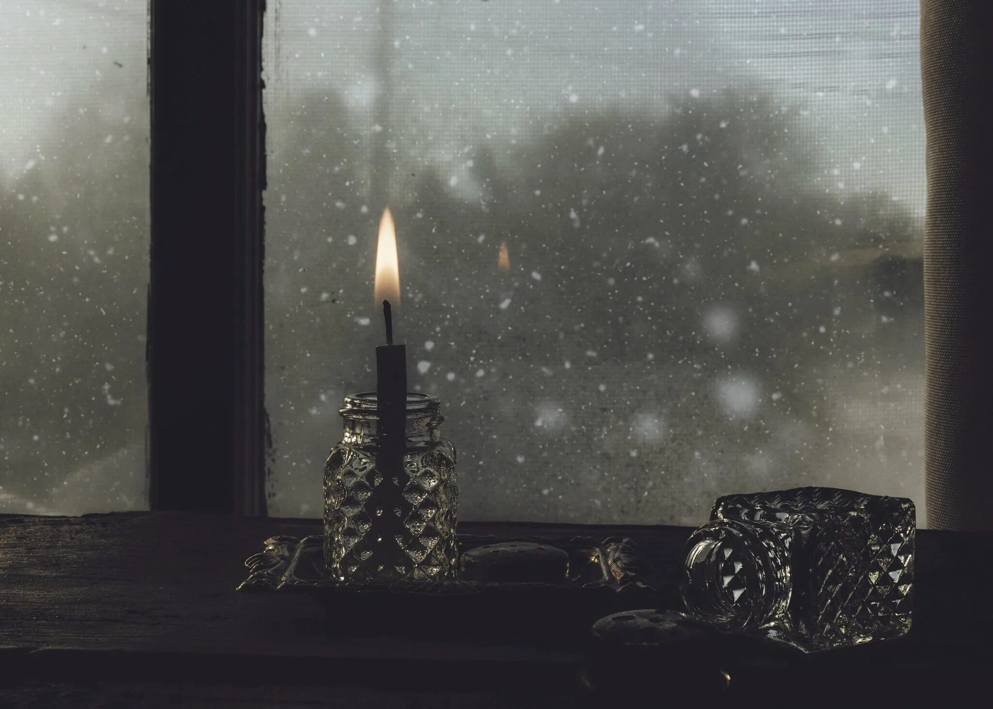 На столе стоит свеча которая отражается. Свеча в окне. Снег за окном. Зима за окном. Свеча горит на окне.