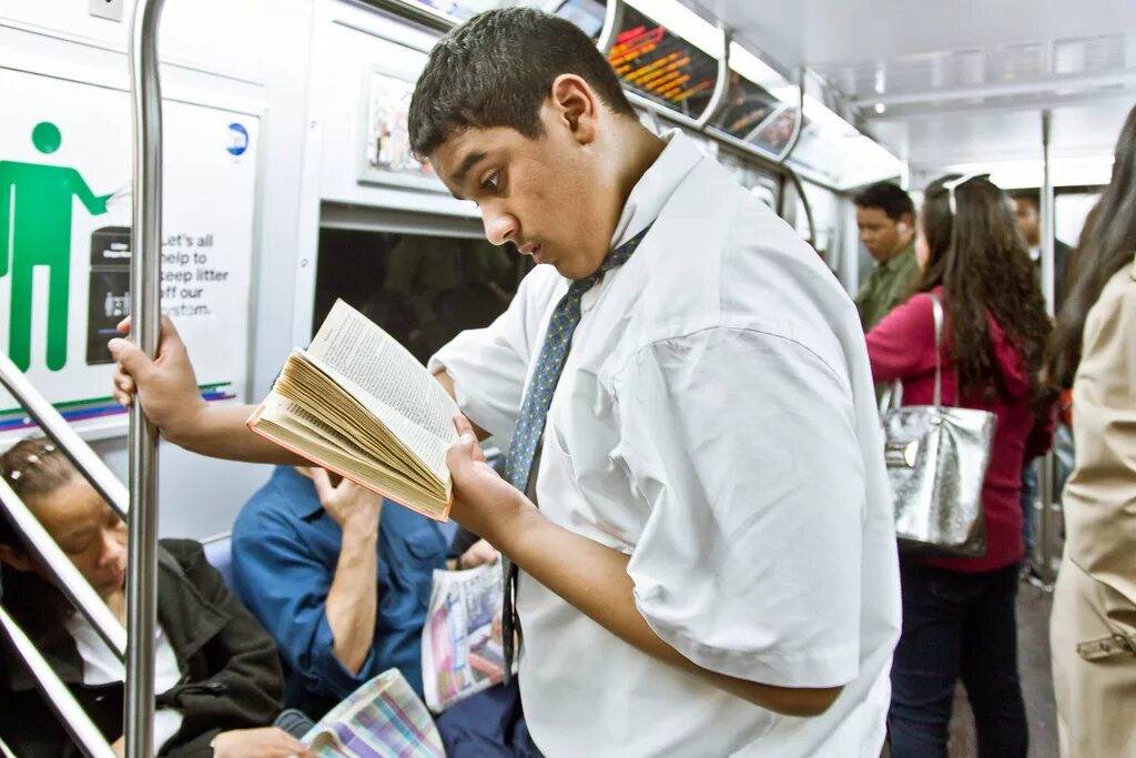 Парень читает книгу в метро. Читает на ходу. Человек читает книгу на ходу. Чтение в странных местах. Она читает в метро