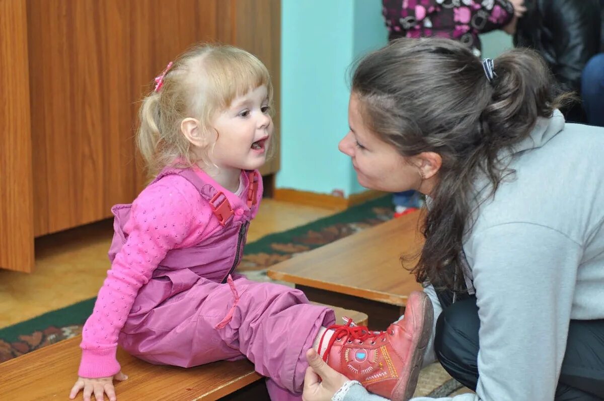 Дочка хочет играть. Мама одевает ребенка в детском саду. Ребенок одевается. Одевание детей в детском саду. Родители одевают детей в саду.