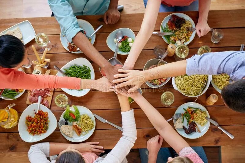 Держусь за стол. Еда объединяет людей. Люди за едой сверху. Руки над столом. Рука с едой.