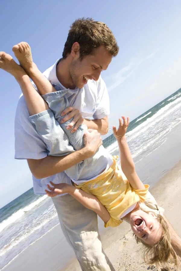 Папа держит дочку на руках. Держит ребенка за ногу на пляже. Папа держит дочь за ногу. Отец держит на руках семью. Папа держит дочку