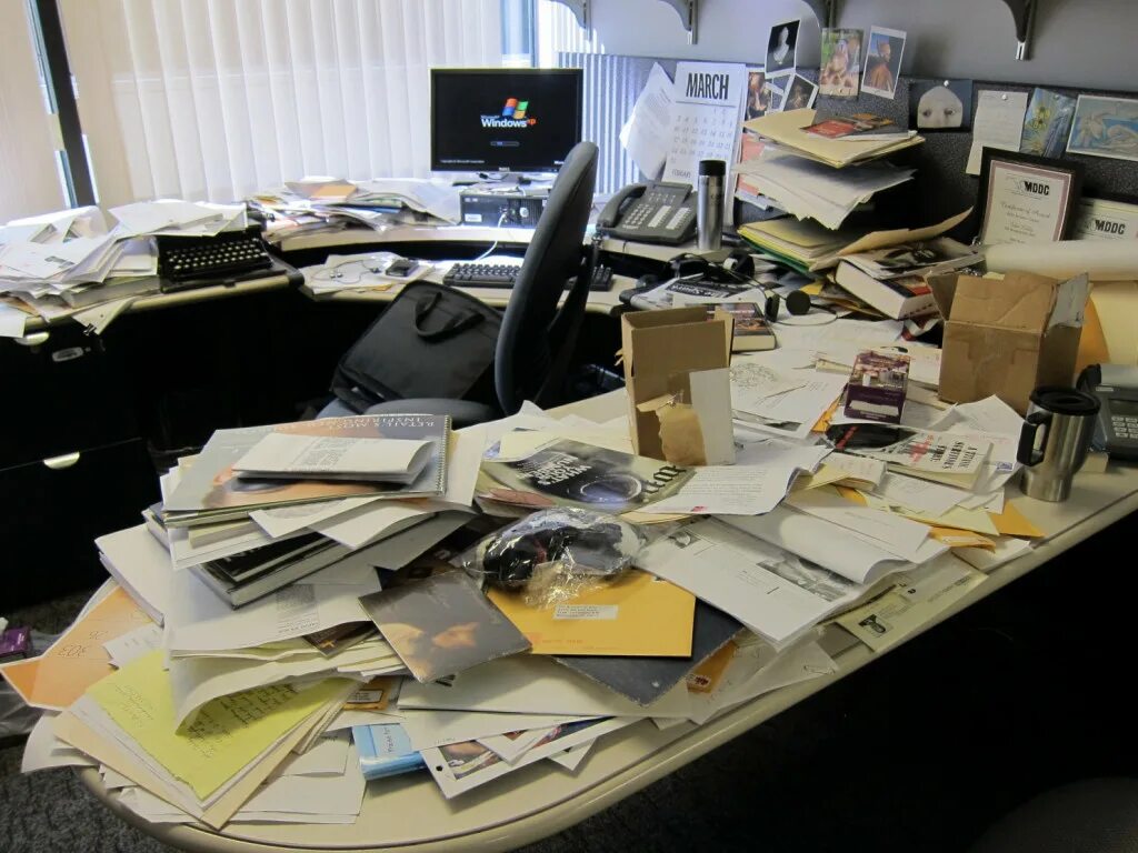 Стол заваленный бумагами. Стол заваленный бумагами в офисе. Бардак на рабочем месте. Беспорядок на офисном столе.